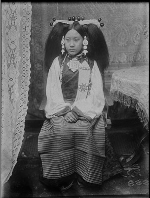 Wife of Lhasa official in gala attire/ The head-dress is mainly of pearls with a few large corals; the earrings of turquoises. The charm-box on the chest is of gold, set with diamonds, rubies, sapphires, and turquoises