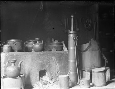 Kitchen utensils. Left, saucepans and teapots; right centre, wooden tea churn and dasher; water bucket on right