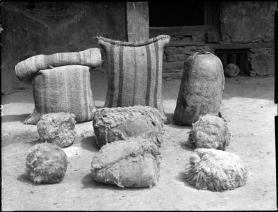 At back, left to right, yak-hair bag of barley flour, yak-hair bag of barley, yak-skin containing rice. In front, six sheepskin bags of butter