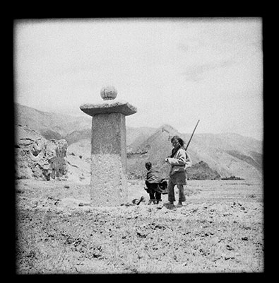 Pillar near mound attributed to Sad-na-legs (Khri Lde-srong-brtsan) which is seen in the background.  Pillar is half buried.  Head of man digging on far side indicates the original height of the pillar.  The south face, seen here, is not inscribed.