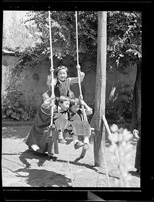 Three girls being pushed on a swing in Dekyi Lingka garden